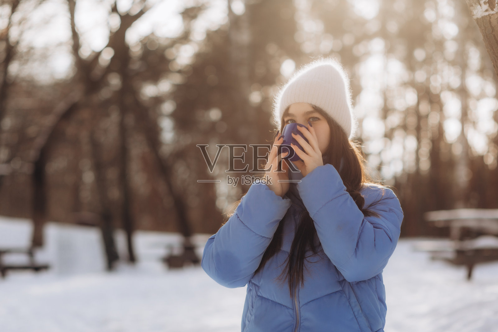 美丽的年轻女子的侧视图,手里拿着一杯热咖啡,闭着眼睛在下雪的公园里。照片摄影图片
