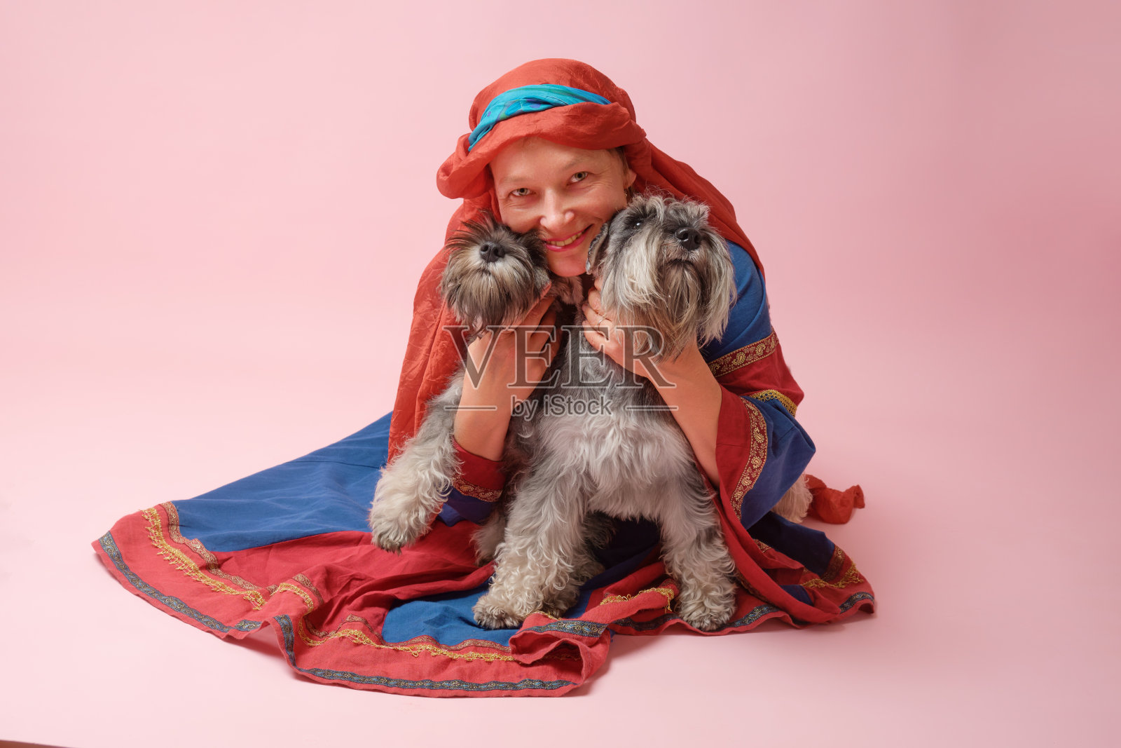 一个女人和她的迷你雪纳瑞犬在一个粉色的工作室里摆姿势拍照。照片摄影图片