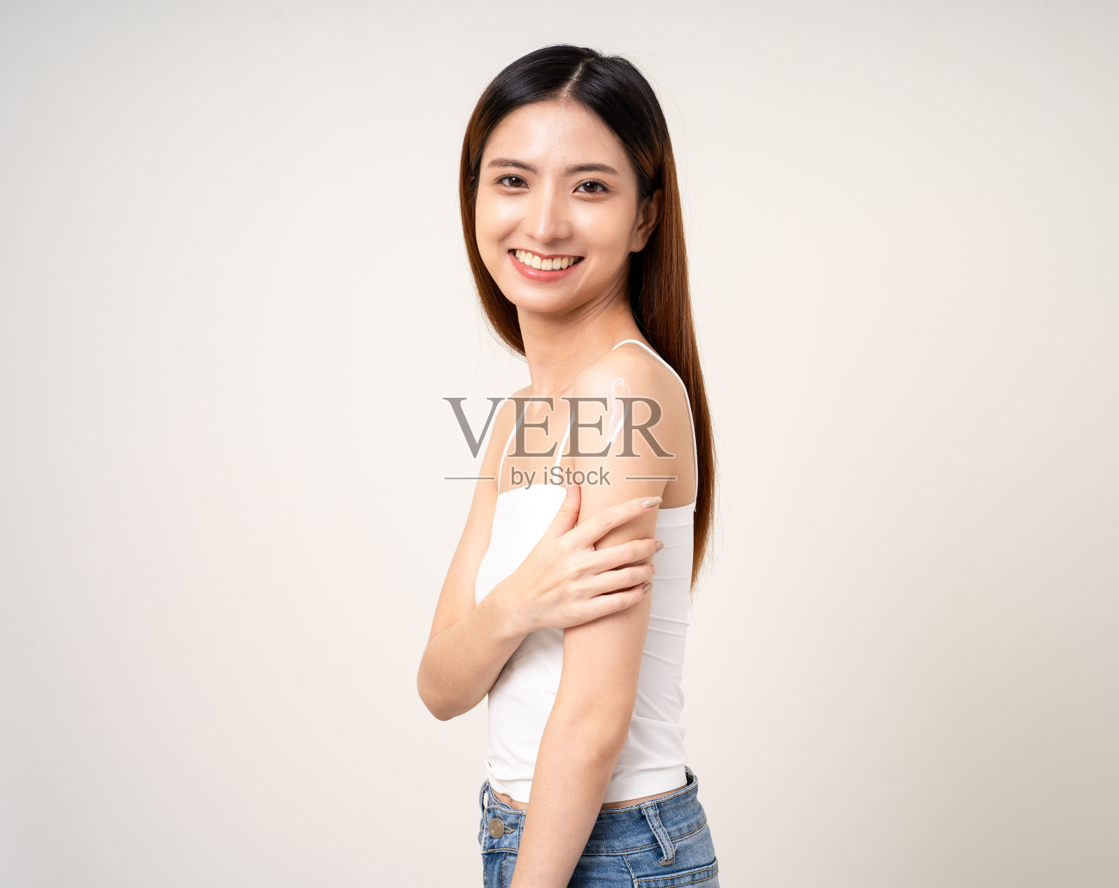 美丽的微笑快乐的年轻亚洲妇女与美容护肤治疗乳液在身体上。迷人的女士站姿涂抹身体乳面部护理美容和水疗照片摄影图片