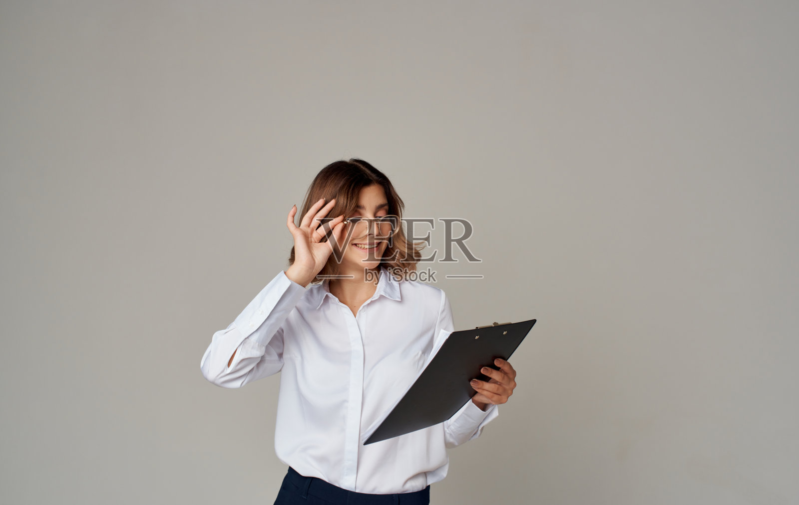 一个灰色背景上拿着记事本、脸上戴着眼镜的女商人用手做着手势照片摄影图片