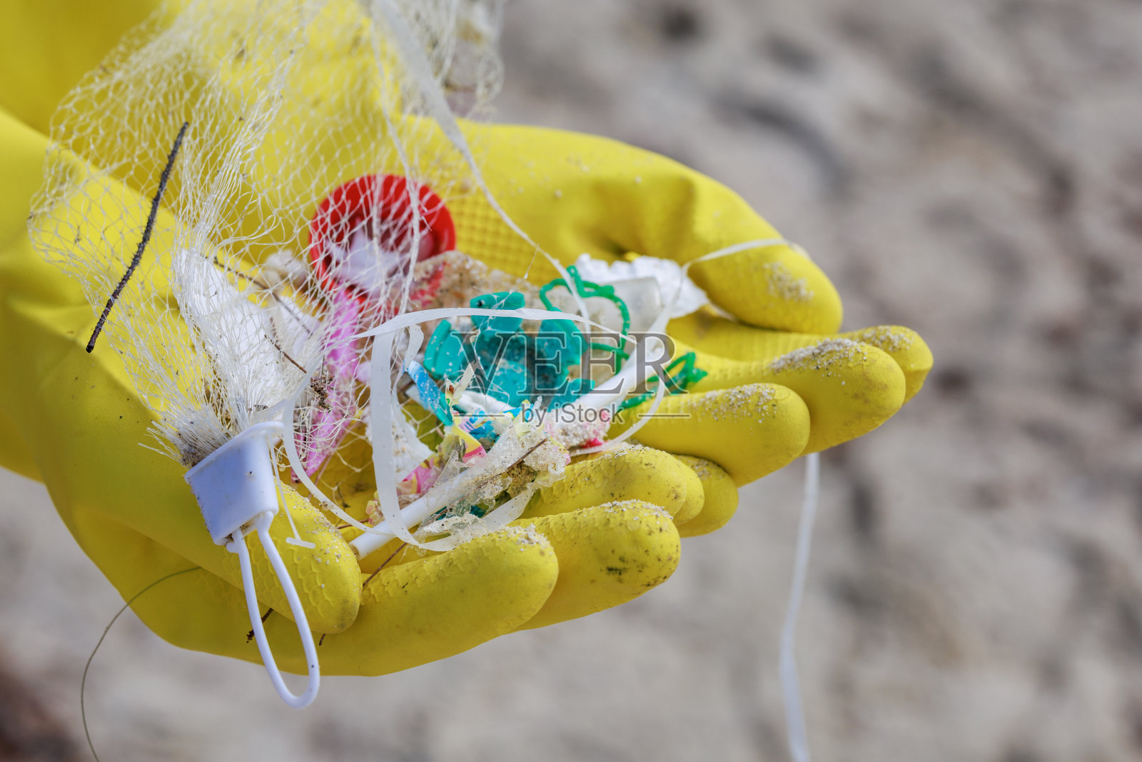 一名研究人员戴着手套,拿着被冲到海滩上的小块塑料污染的特写照片,突显了海洋环境中塑料污染的持续问题照片摄影图片