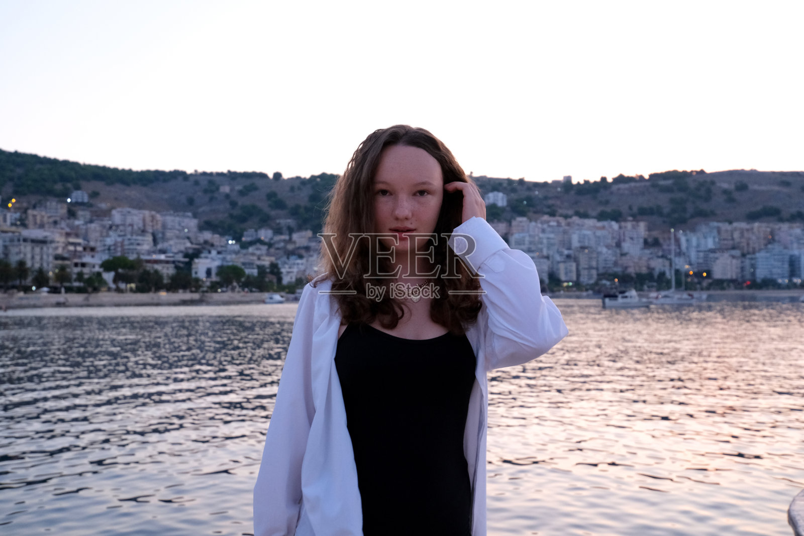 可爱的女孩在镜头前摆出甜美的姿势,慢慢地走近水岸,眯着眼睛欣赏周围不可思议的风景,站在海滩上照片摄影图片