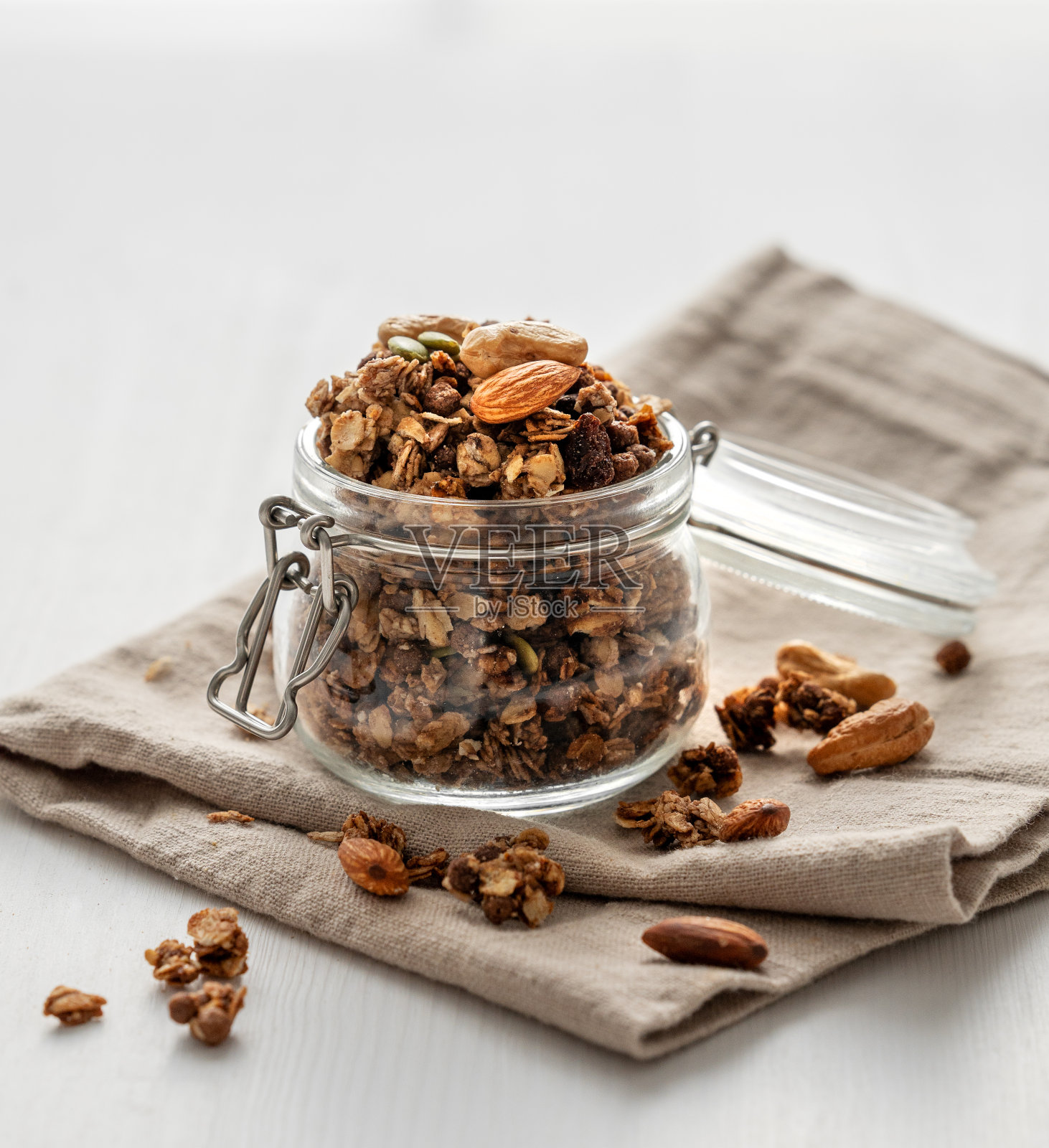 自制的格兰诺拉燕麦卷装在白色背景的罐子里,上面有坚果和餐巾。舒适的食物。照片摄影图片