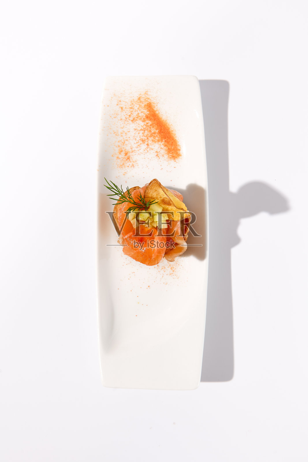 在明亮的环境中,白色的陶瓷拼盘上放着鲑鱼profiterole,上面撒着一层有创意的辣椒粉照片摄影图片