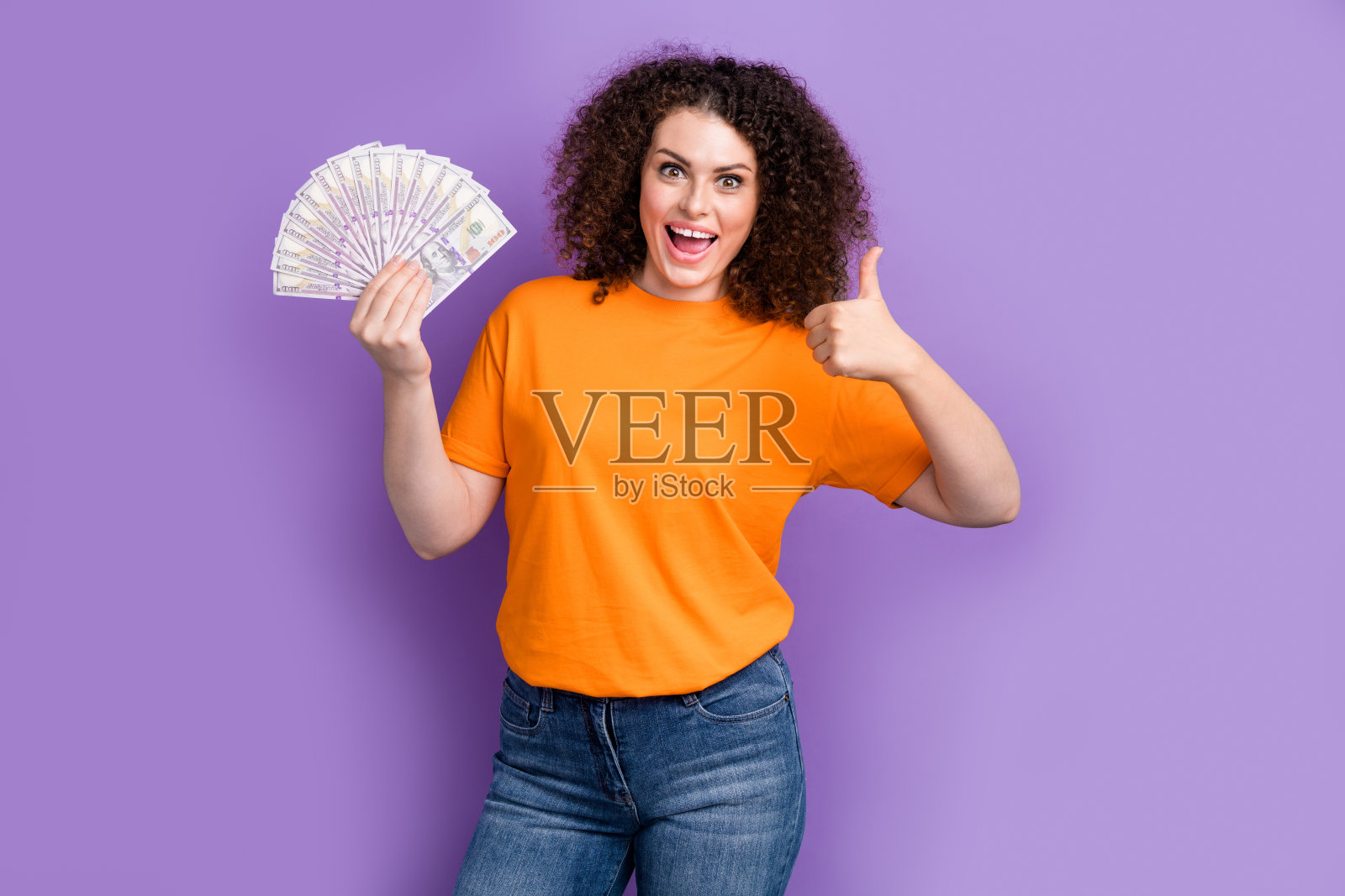 照片积极兴奋的女士穿着橙色t恤显示拇指上升现金风扇孤立的紫色背景照片摄影图片