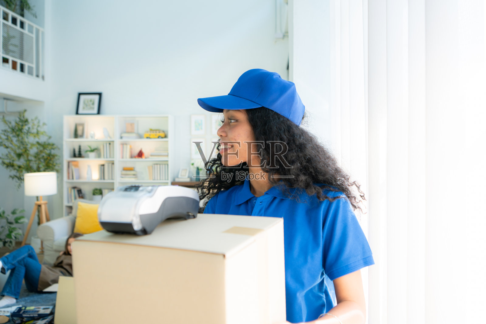 微笑的送货女拿着盒子,看着家里的照相机照片摄影图片