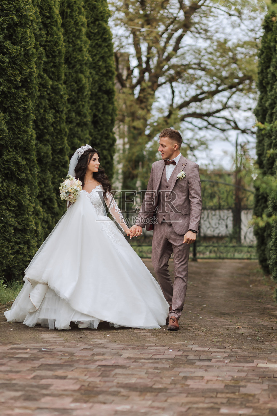 婚礼结束后,年轻的新娘和新郎走在春天公园的鹅卵石上。新婚夫妇快乐,复印空间。照片摄影图片