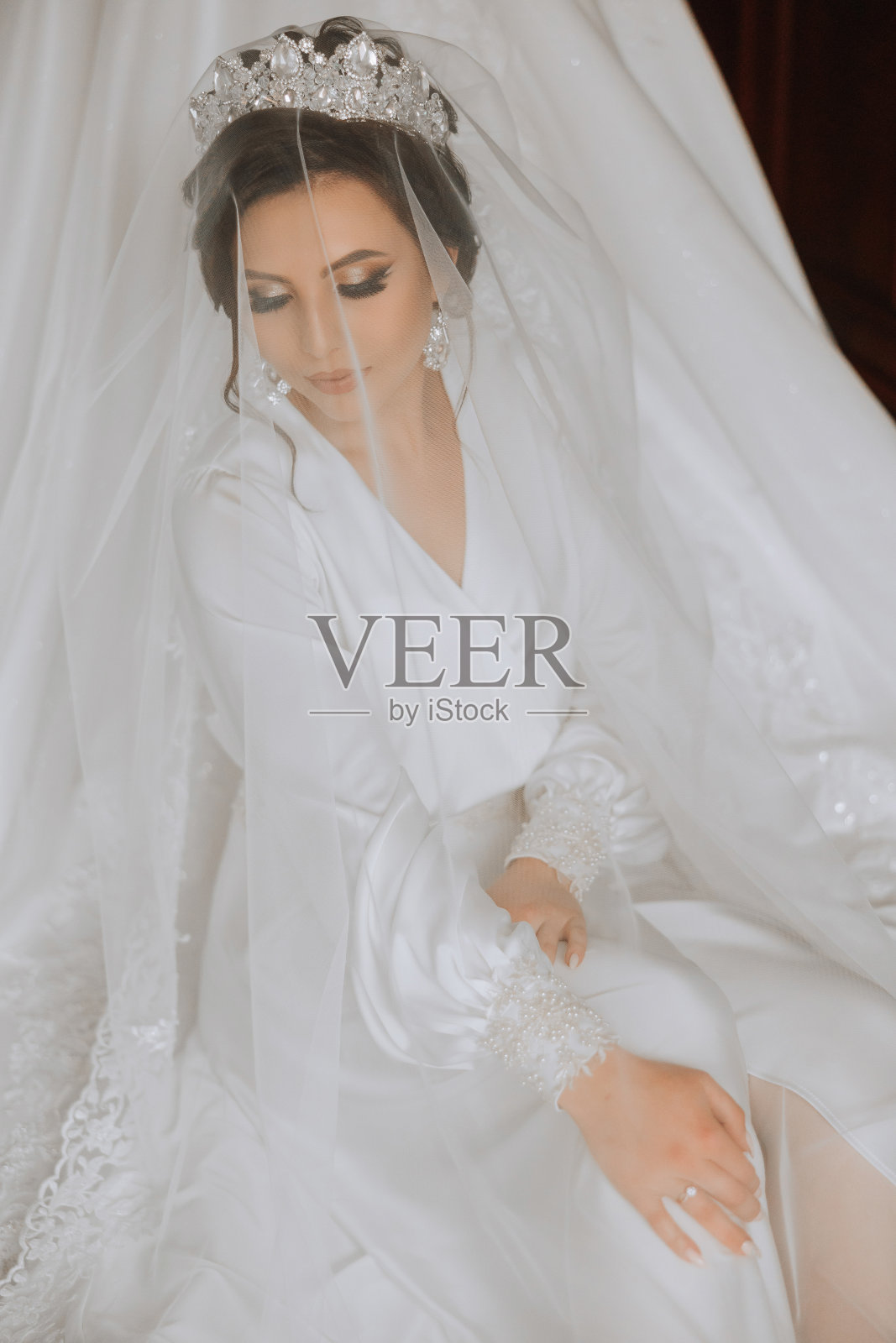 一位快乐的新娘正在酒店房间里准备她奢华的婚礼,旁边的假人身上穿着一件婚纱。一个女人的肖像,时髦的头发,化妆和微笑,穿着晨衣。照片摄影图片