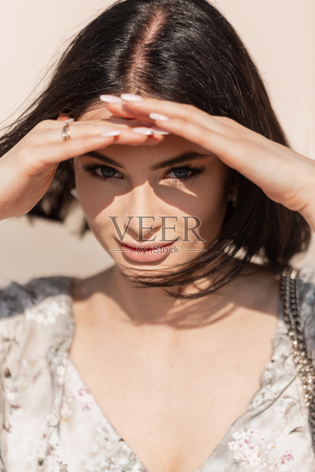 在一个阳光明媚的夏日,一个有着漂亮脸蛋和蓝眼睛的时尚美女,穿着时尚的裙子,用手遮住眼睛,看着镜头照片摄影图片