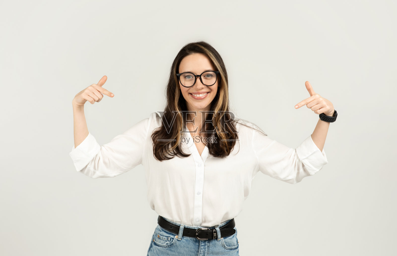 穿着一件白衬衫,戴着眼镜的黑发女人用大拇指指着自己照片摄影图片