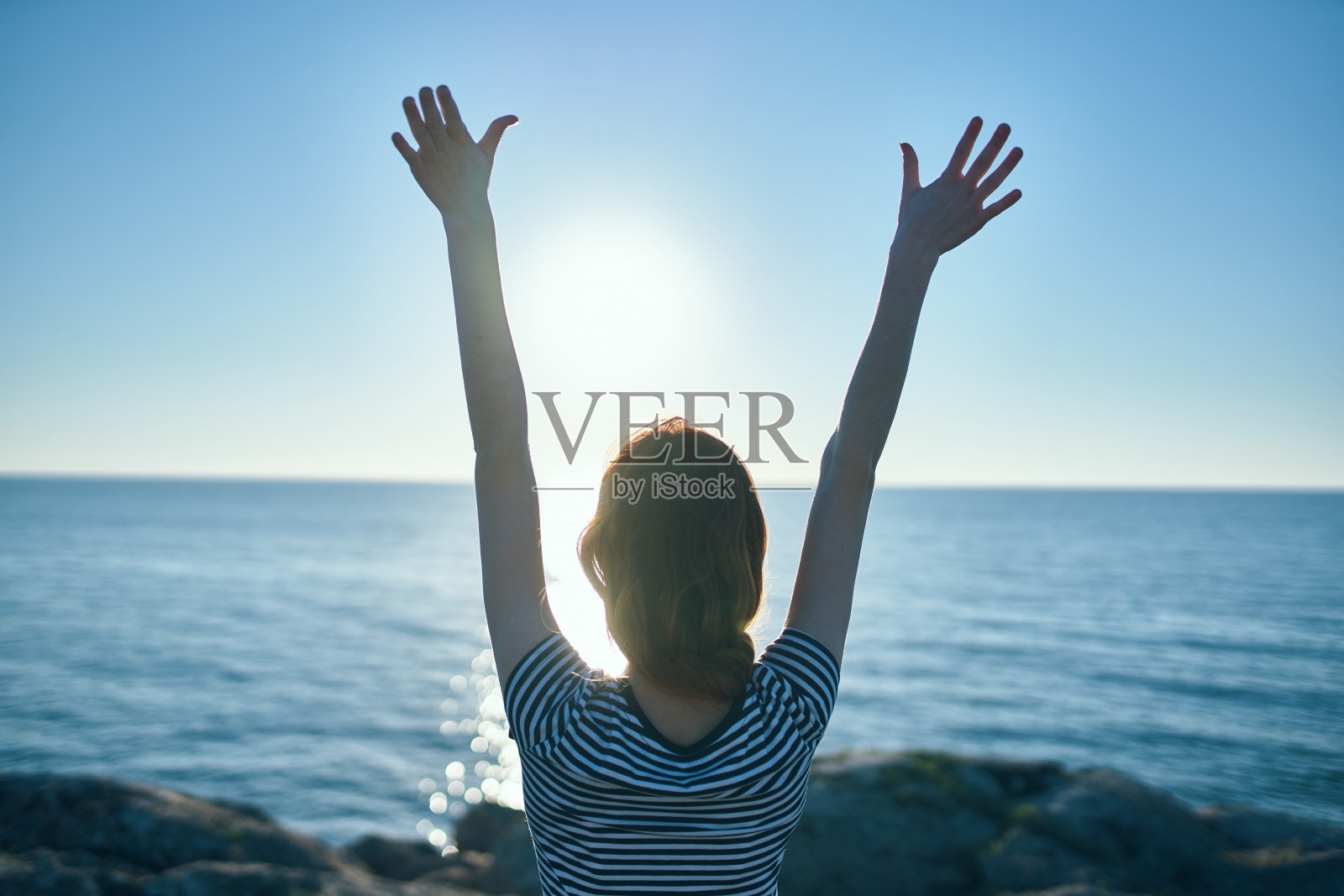 女人在日落时在山上举手看日落时在海边照片摄影图片