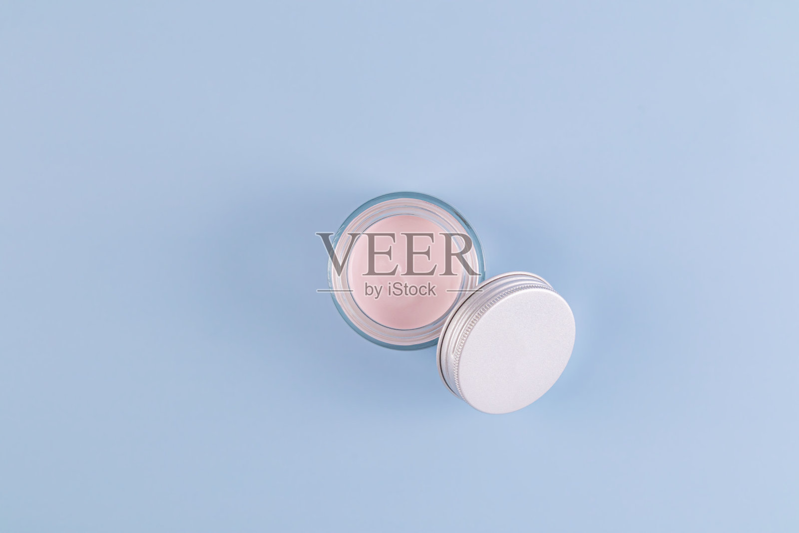 打开玻璃透明罐粉红色乳霜为年轻皮肤的脸和身体在蓝色背景与复制空间。天然的化妆品。照片摄影图片