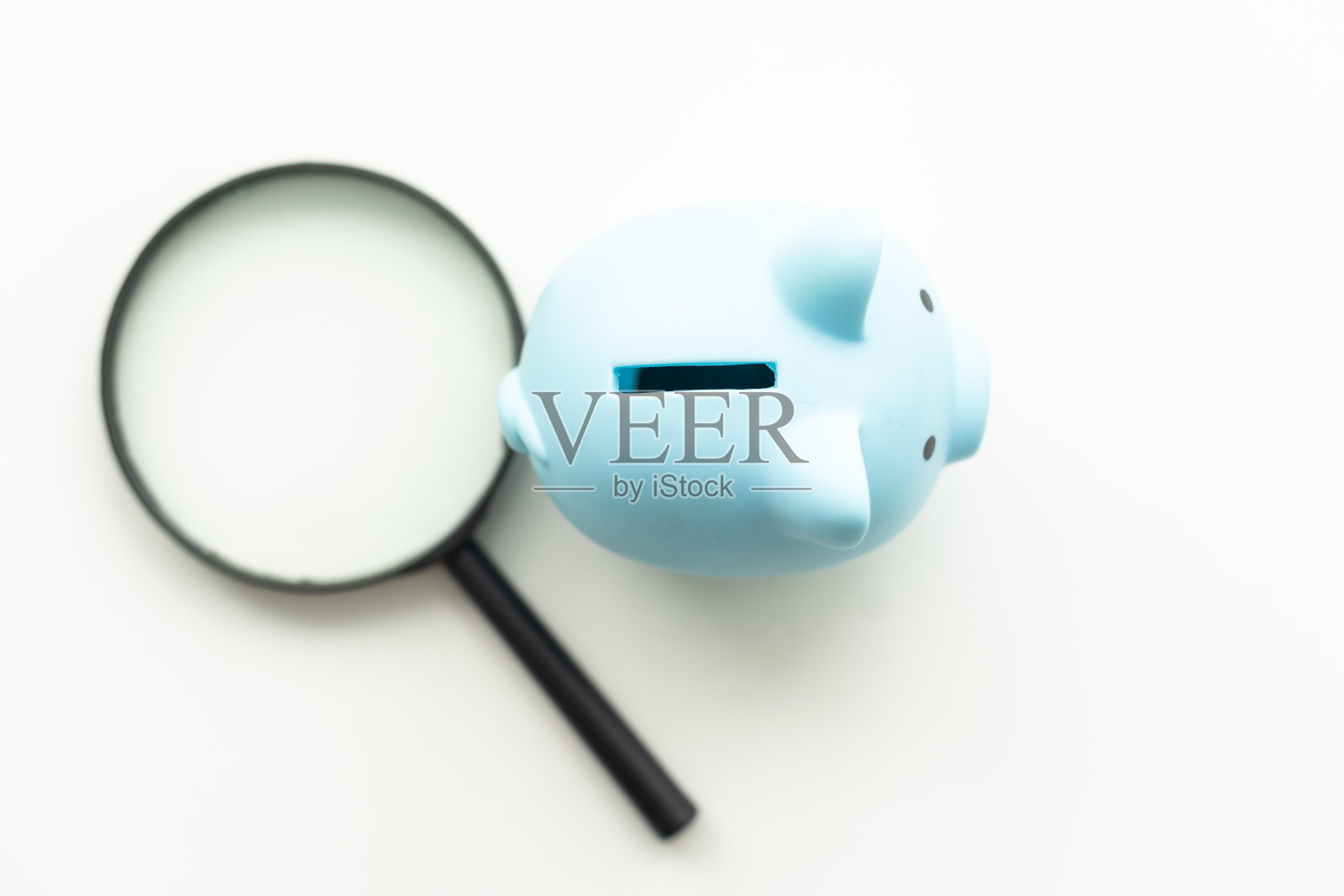 灰色背景上的放大镜和粉色储蓄罐。照片摄影图片