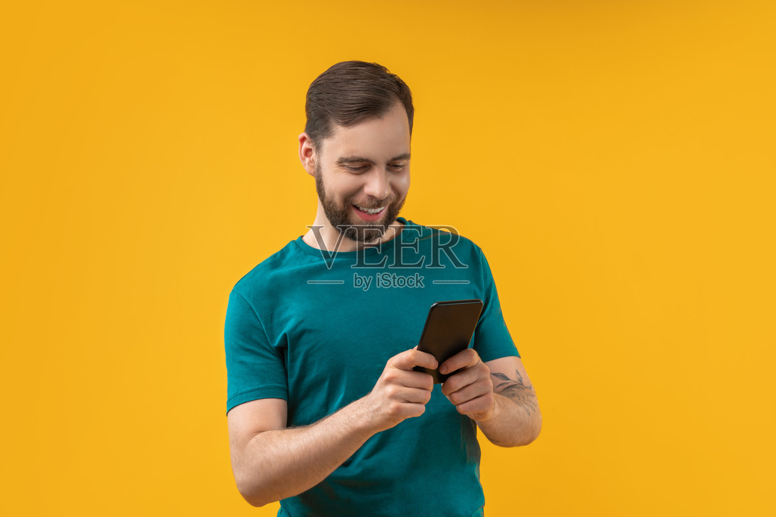 一名满脸笑容的大胡子男子在工作室里用他的智能手机在博彩公司的网站上用手机应用下注照片摄影图片