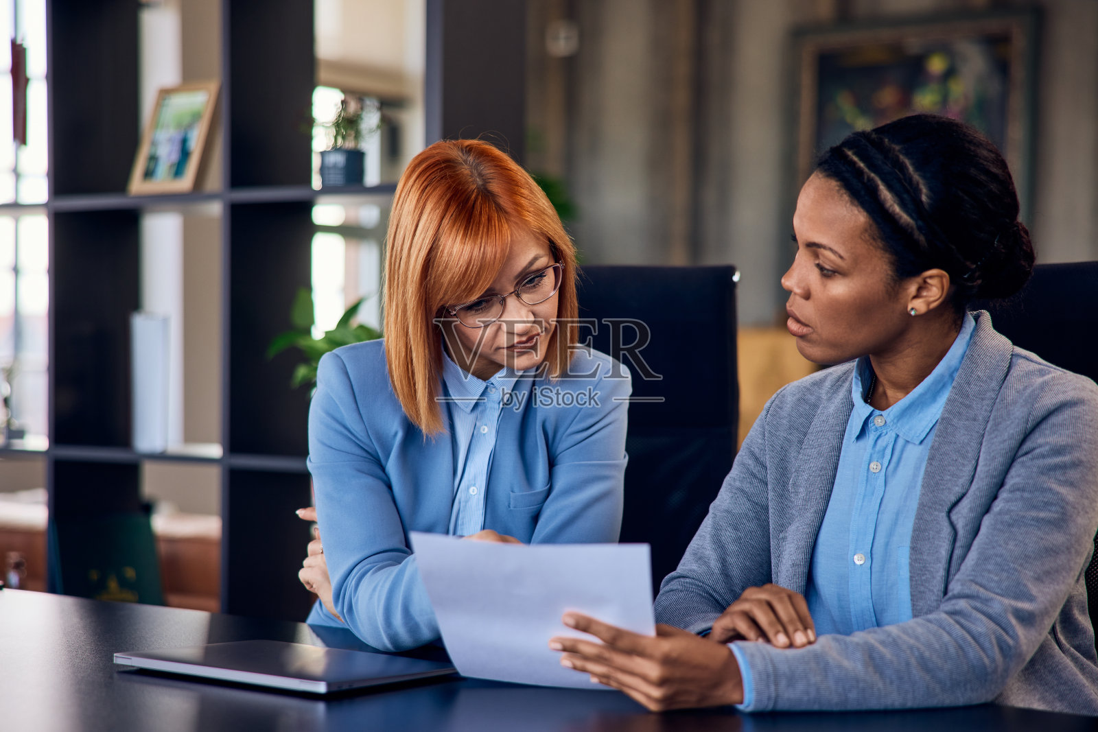两个专注的女性,一起在办公室工作,看着一份文件。照片摄影图片