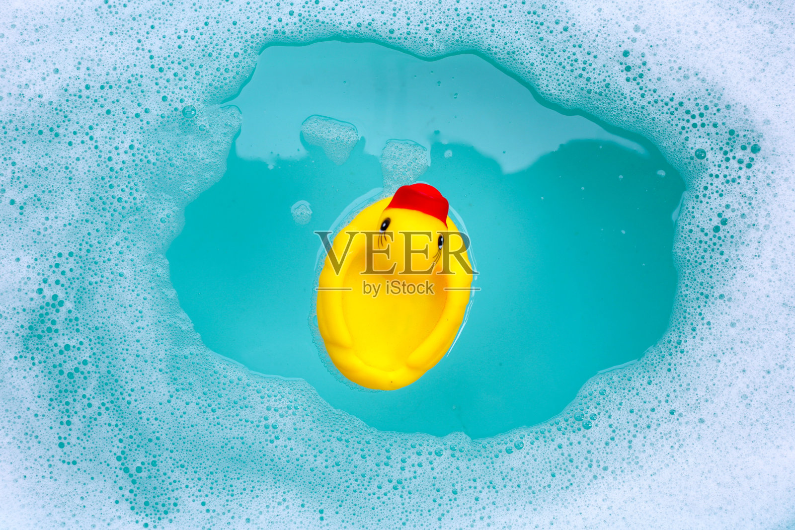 黄色的鸭子橡皮玩具,在蓝色的盆里有泡沫照片摄影图片