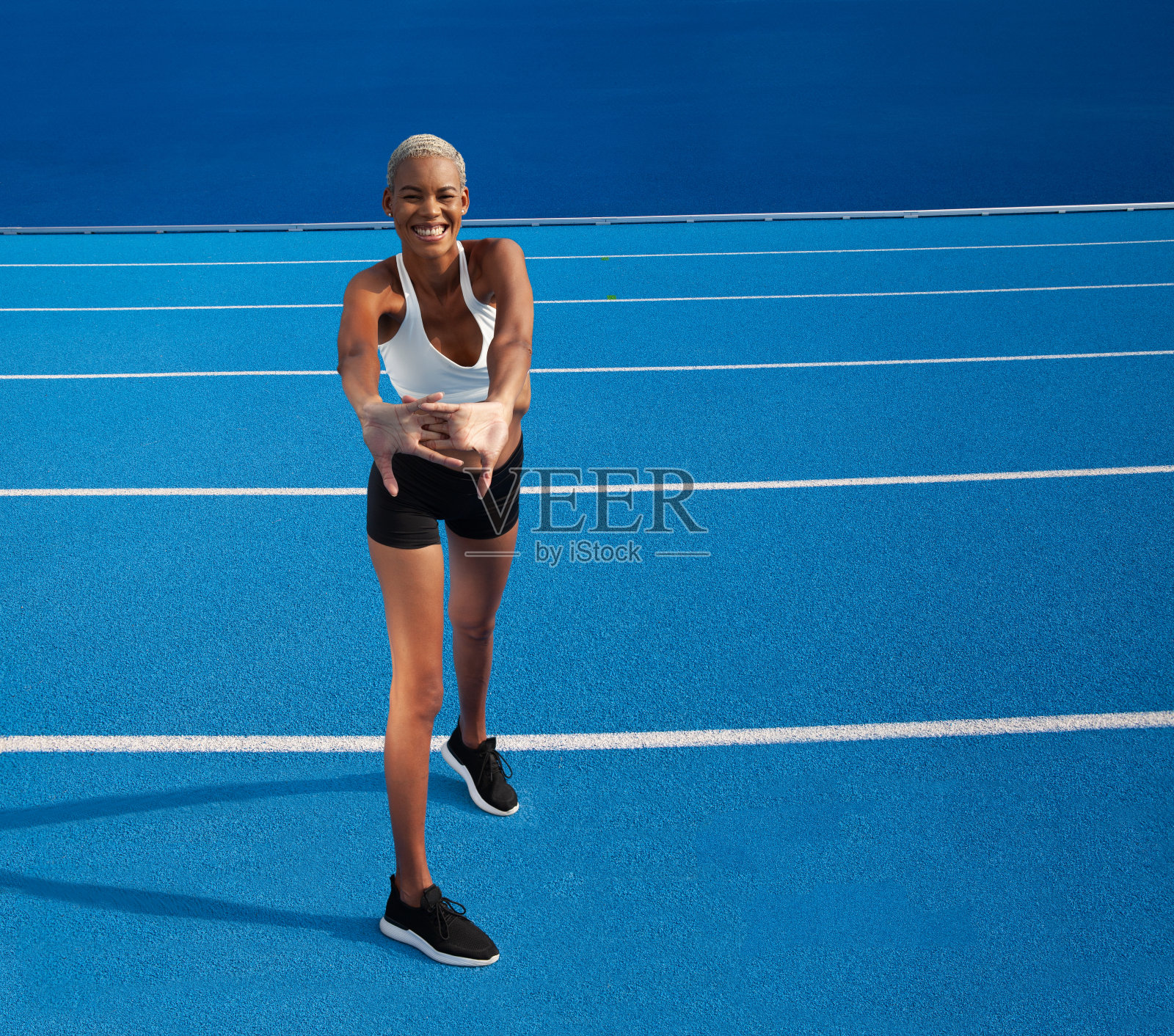 一位非裔美国女运动员在奥林匹克蓝色跑道上进行热身运动,体现了赛跑训练和体育奉献的理念照片摄影图片