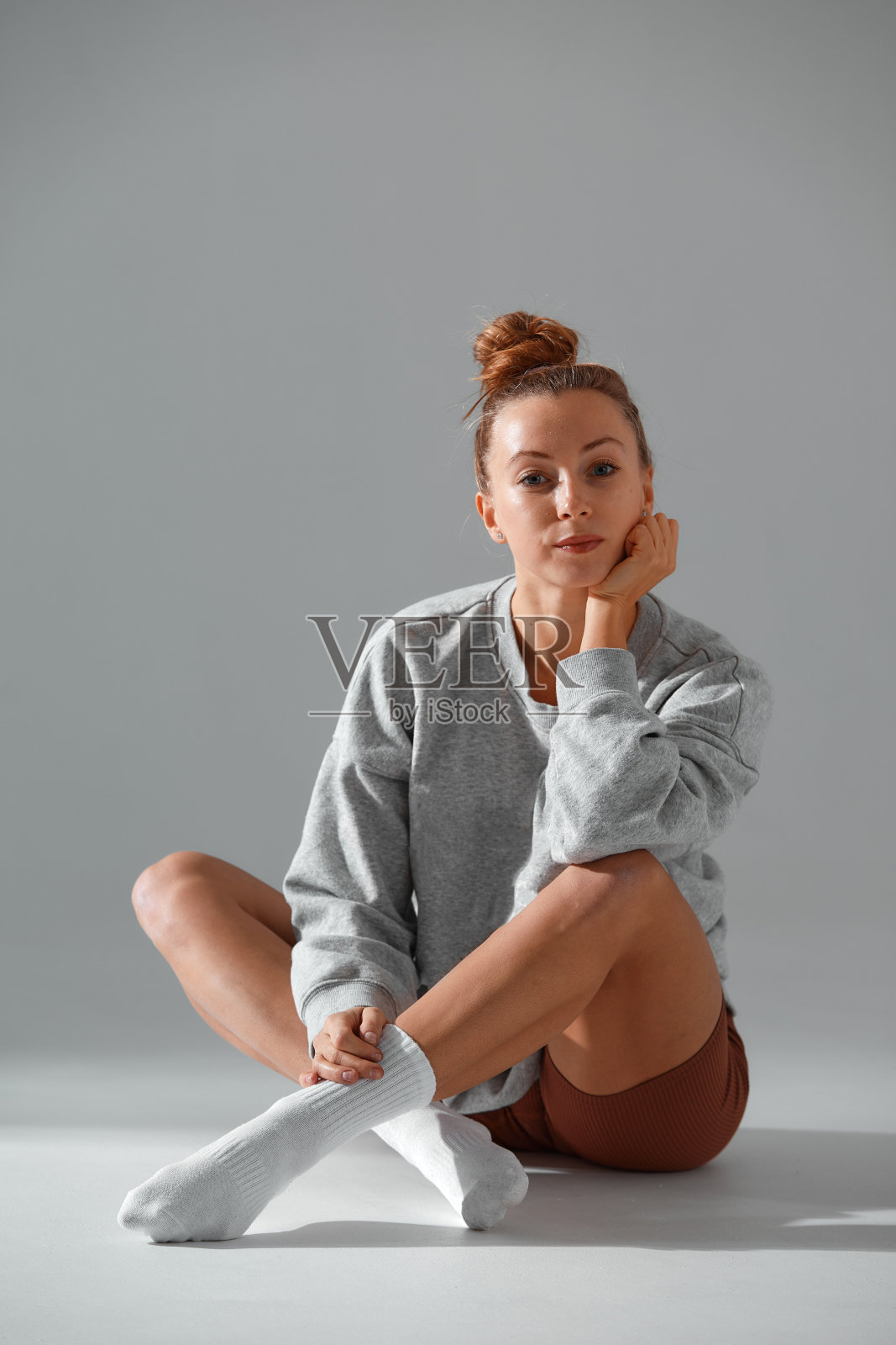 健身女模特在时尚运动服放松灰色背景。穿着时尚运动服的性感女孩坐在工作室里的全身肖像照片摄影图片