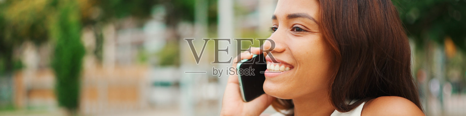 美丽的女孩,黑色长发,穿着白色上衣,坐在城市公园的长椅上,使用手机全景。年轻女子在打电话照片摄影图片