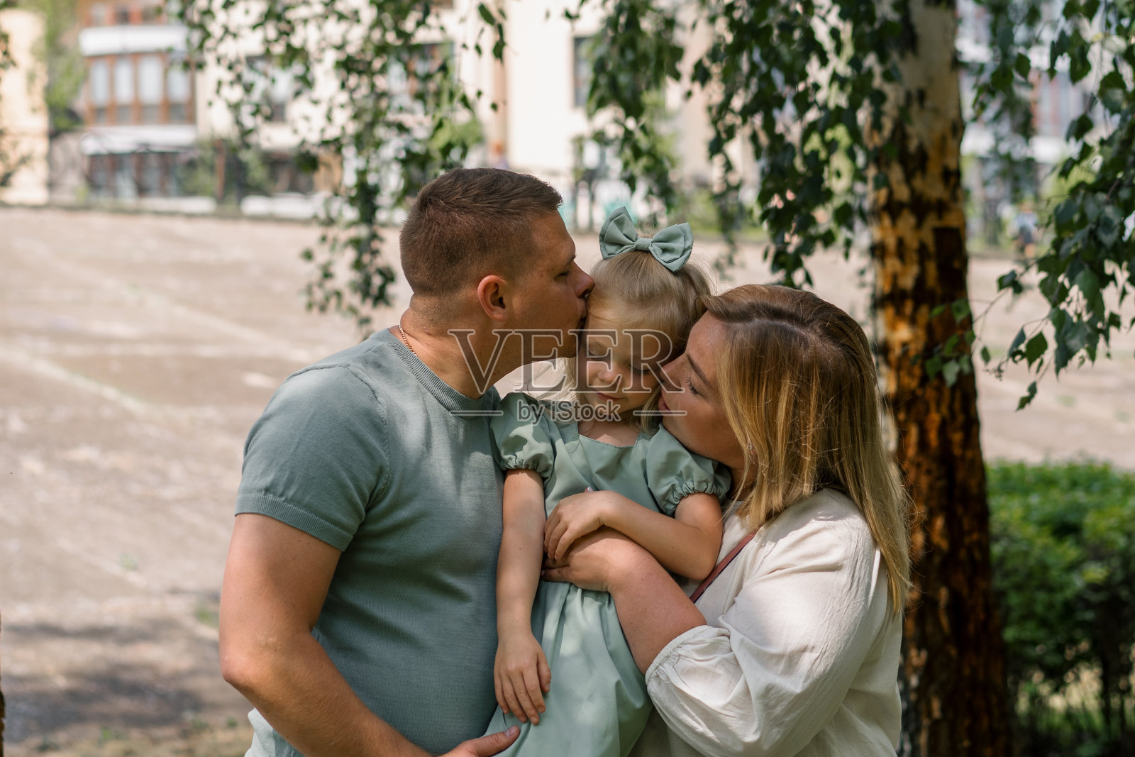 一个幸福的年轻家庭的肖像,妈妈,爸爸和女儿父母抱着一个女婴在他们的怀里,亲吻她的家人在公园散步的童年照片摄影图片