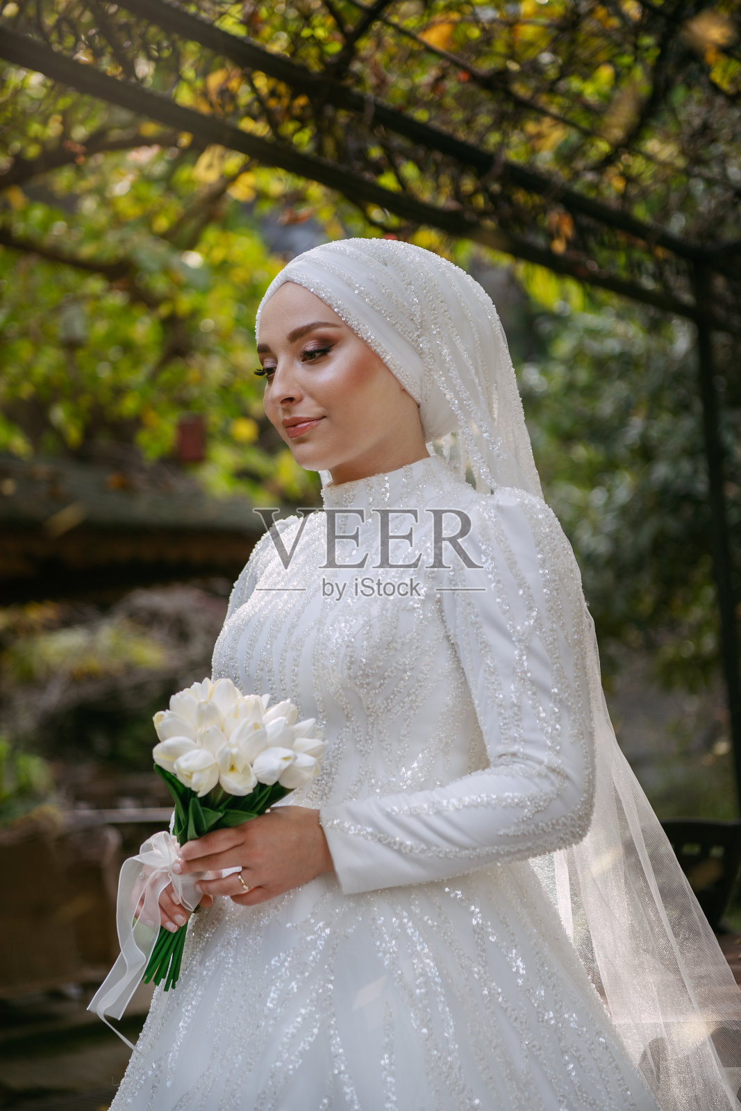 身穿白色蕾丝婚纱的年轻新娘手持白色郁金香婚礼花束在户外摆姿势照片摄影图片