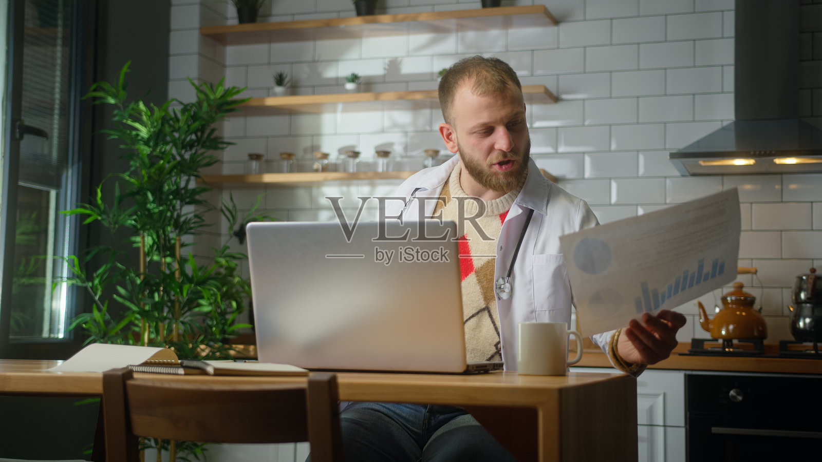 穿着白大褂的忙碌医生在家里办公室用笔记本电脑研究病人报告。做文书工作的男医生照片摄影图片