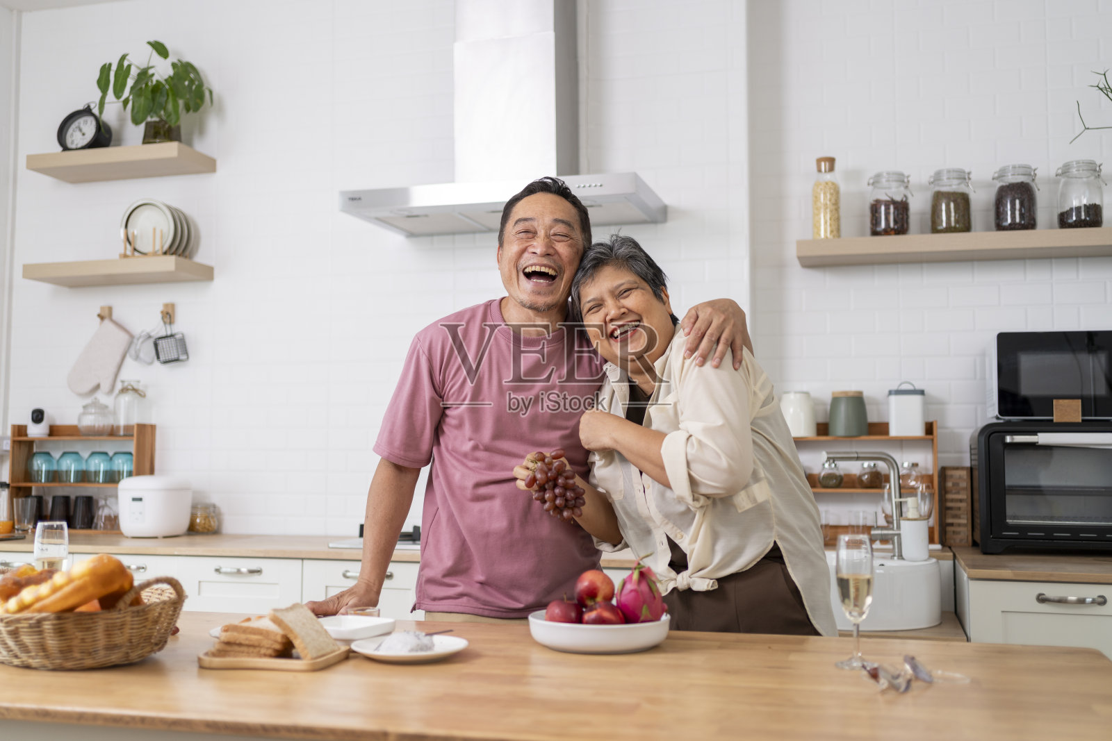 成熟的亚洲夫妇在厨房里用葡萄开玩笑。照片摄影图片