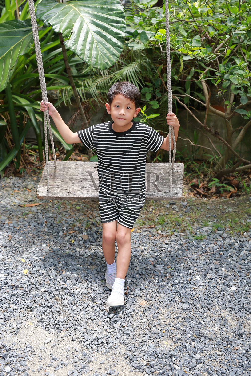 亚洲小男孩的肖像,孩子们坐在花园里的秋千上玩耍。照片摄影图片
