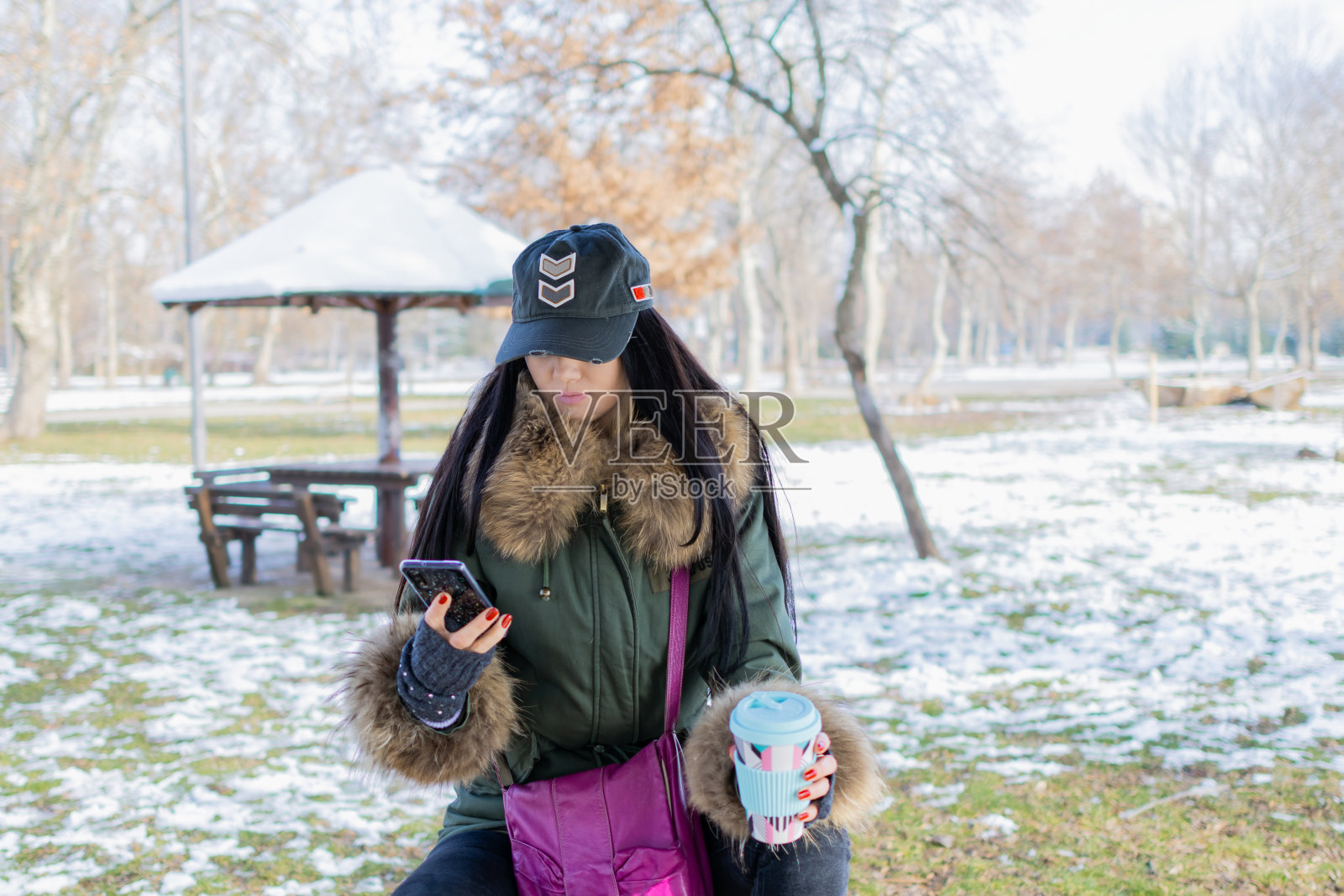 在一个下雪的冬日,一位美丽的年轻女子在公园里享受着她的咖啡。她在自拍,或者视频通话。照片摄影图片