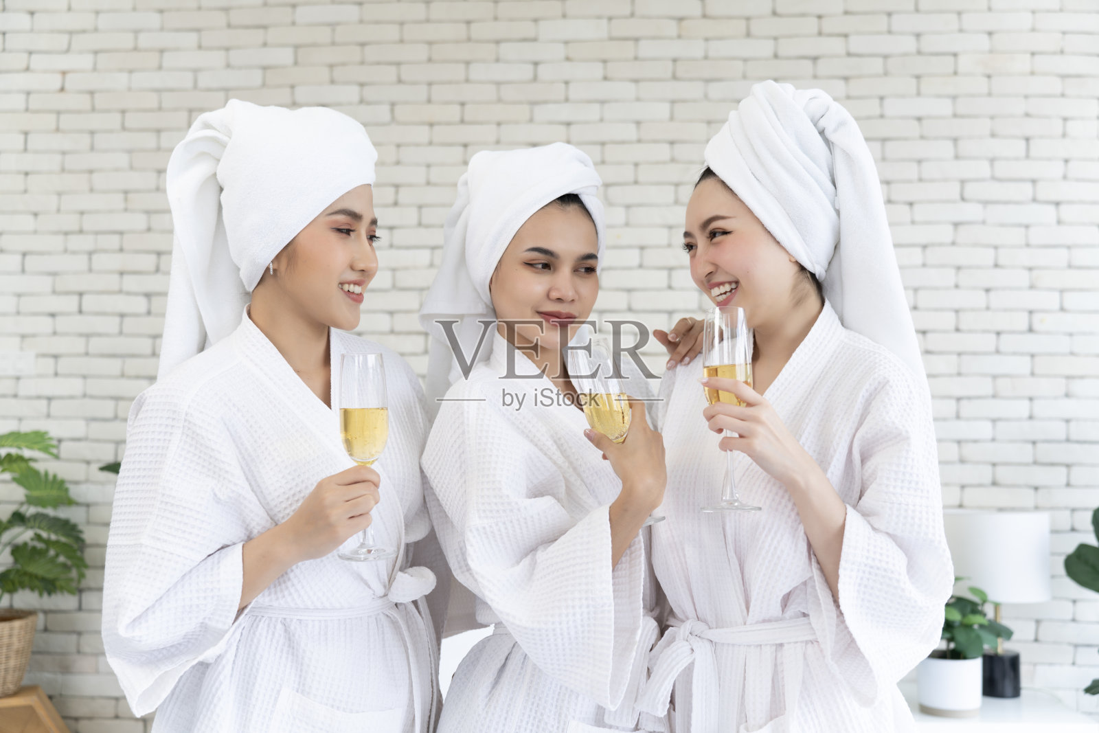 三个穿着浴袍、手拿酒杯的年轻女子站在卧室里聊天照片摄影图片