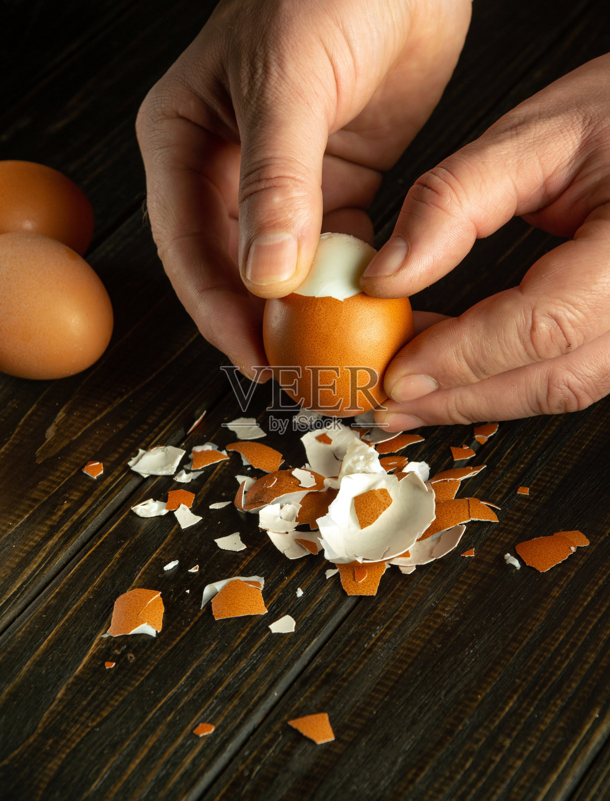厨师用手剥开煮熟的鸡蛋,准备餐桌上的一道国菜。用于铭文或广告的黑暗场所照片摄影图片