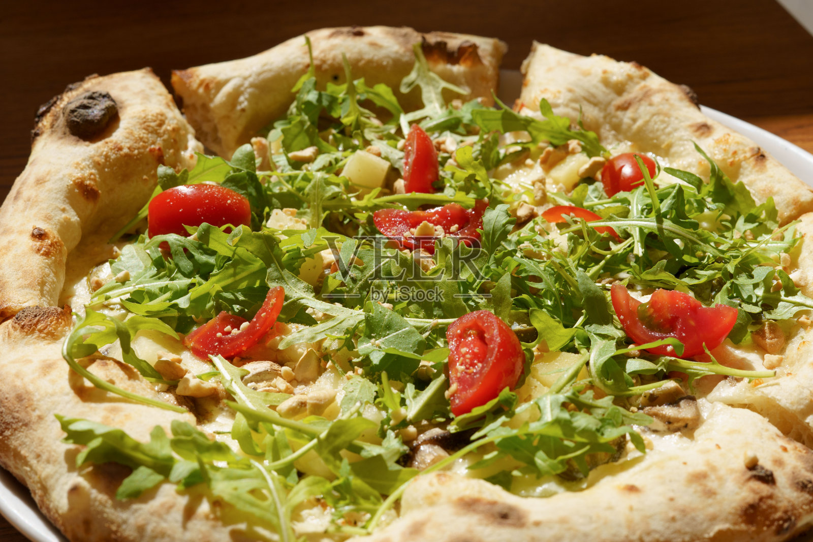 阳光直射下多汁酸面团披萨配芝麻菜和西红柿的特写。美食的概念,小吃,烹饪食谱照片摄影图片