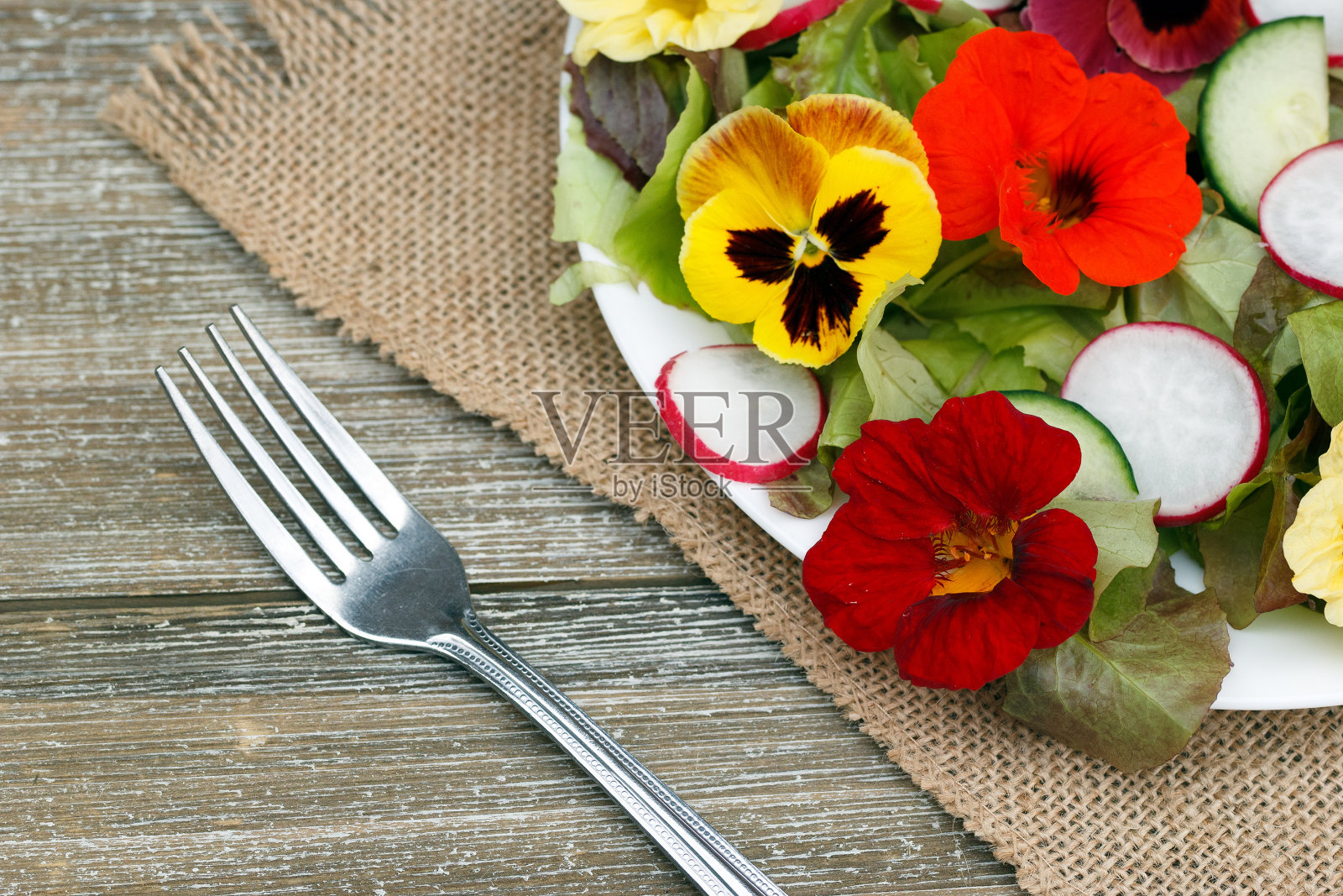 木桌上有鲜花、萝卜和生菜的素食沙拉。照片摄影图片