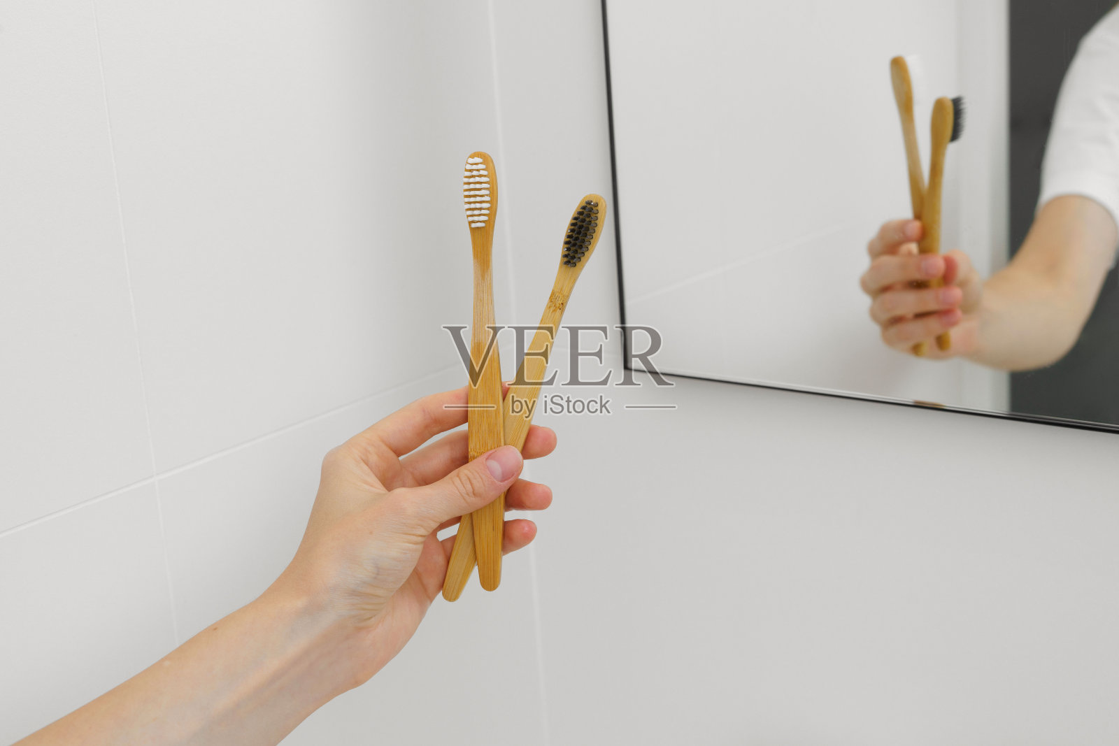 浴室里镜子的背景上,一位年轻女子手里拿着两把天然的木制竹制牙刷。口腔护理理念,美容产品,可持续生活方式,零浪费家园照片摄影图片