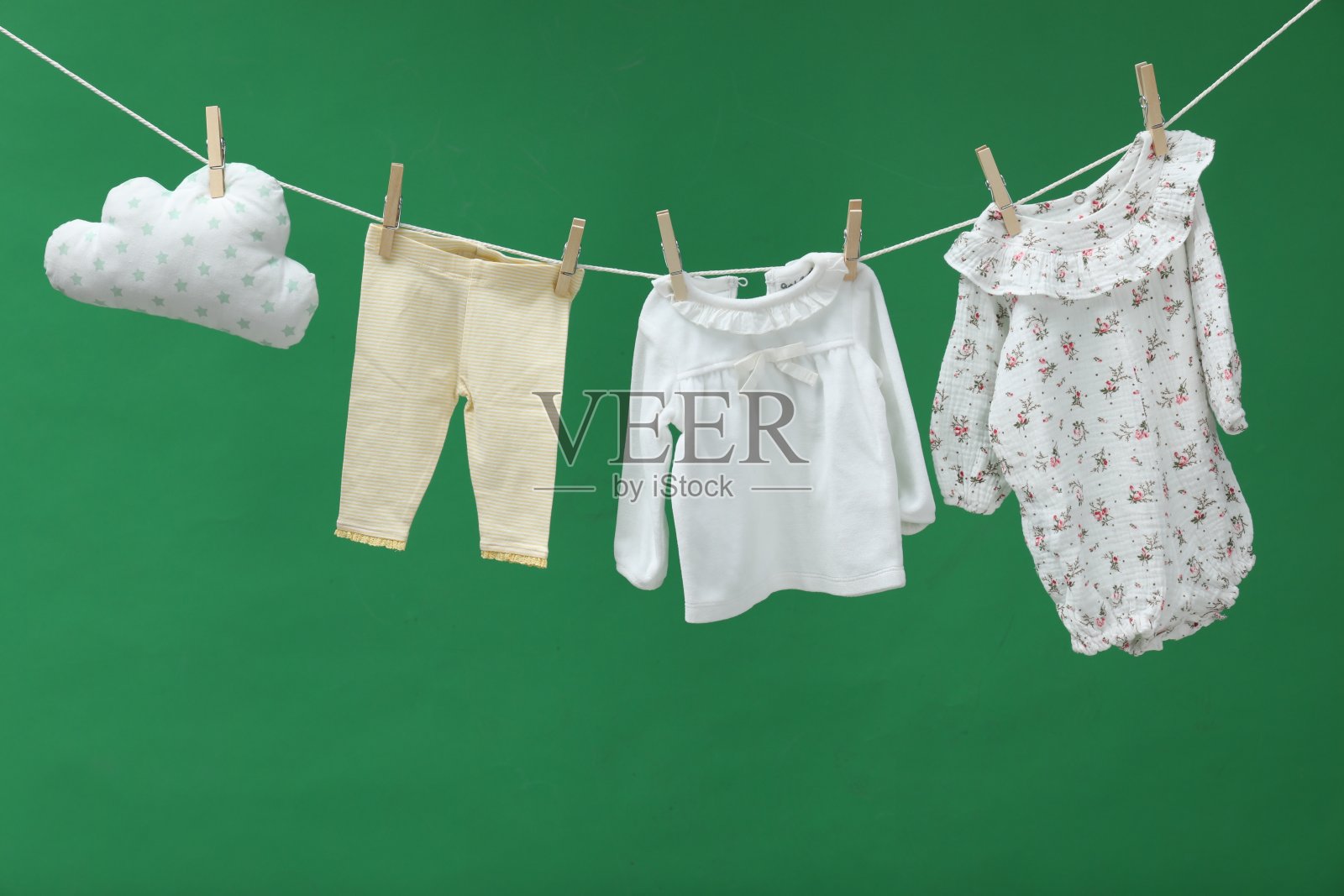 不同的婴儿服装和云状枕头在绿色背景下晾晒照片摄影图片