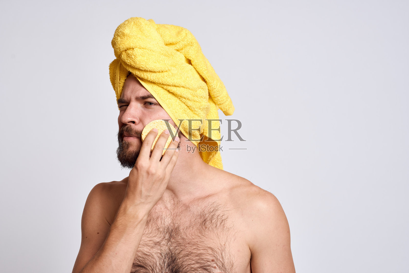 男人用黄色毛巾在头上,裸露的肩膀,海绵清洁皮肤,面部护理光背景照片摄影图片