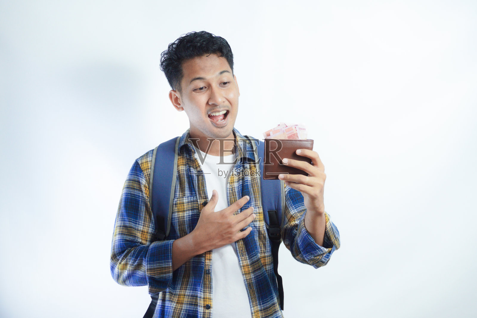 兴奋的年轻亚洲学生男子穿着休闲服,背着背包,拿着装满现金的钱包,孤立在白色背景上。高中教育大学学院理念照片摄影图片