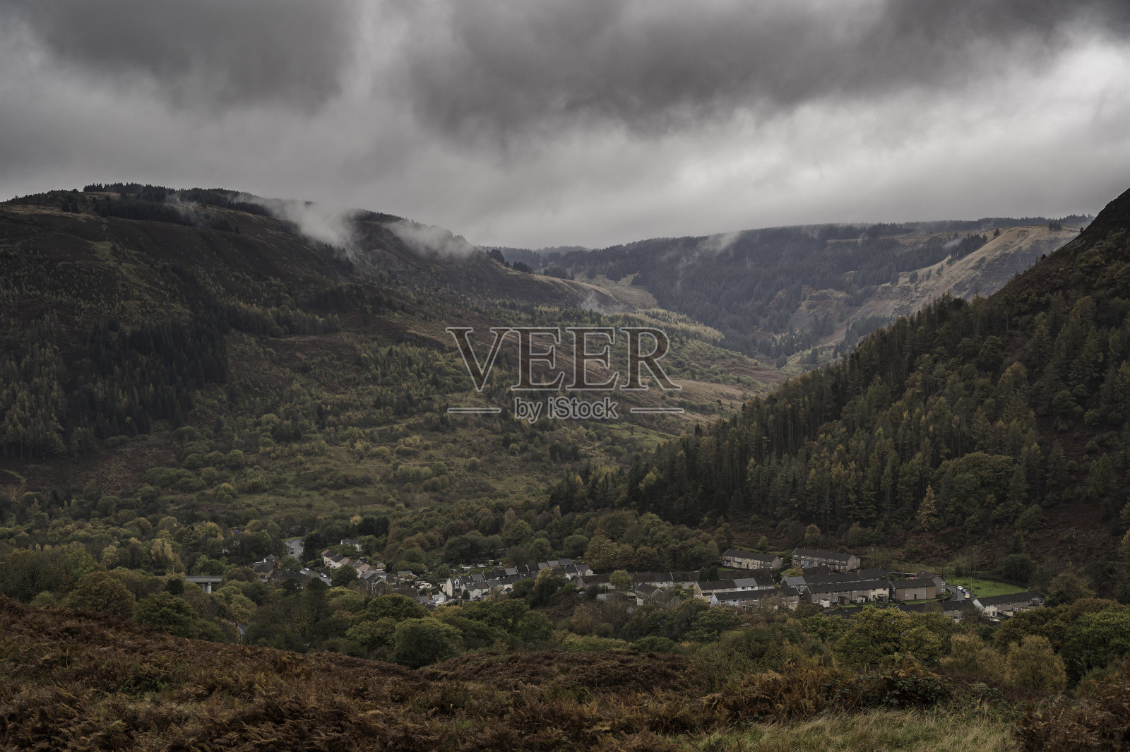 秋天的一天,南威尔士朗达山谷山顶上的景色,云层低垂在山顶上。在山脚下可以看到一个小社区照片摄影图片