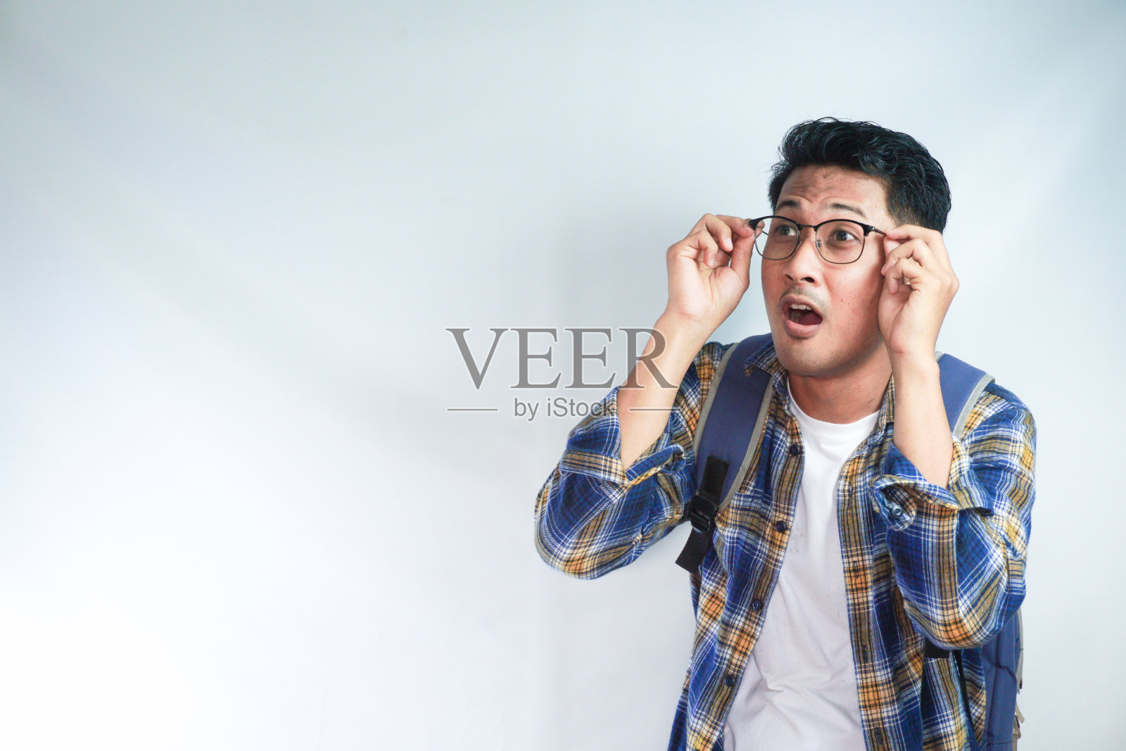 兴奋的年轻亚洲男学生,穿着休闲服,背着眼镜,在工作区的模型上看向一边,孤立在白色的背景上。教育在高中大学学院的概念照片摄影图片