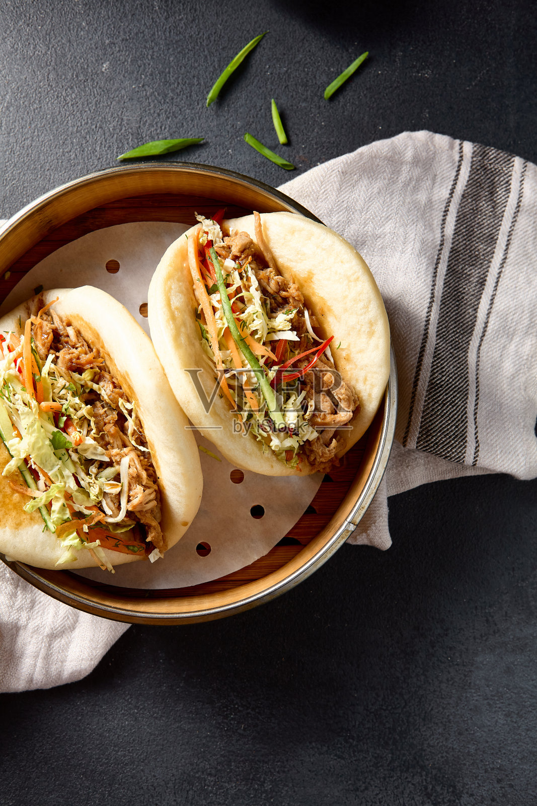 头顶上的包馍,里面装满了猪肉丝和蔬菜,在深色的表面上点缀着新鲜的草药照片摄影图片