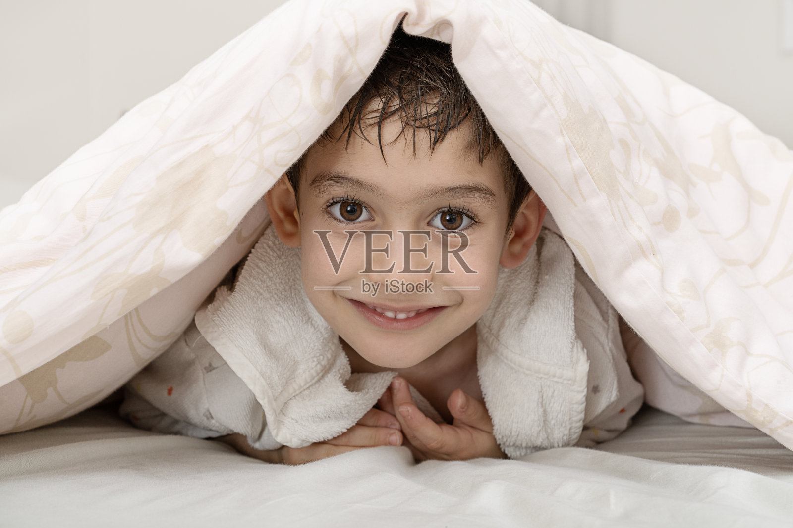 毯子下微笑的小男孩的肖像。照片摄影图片