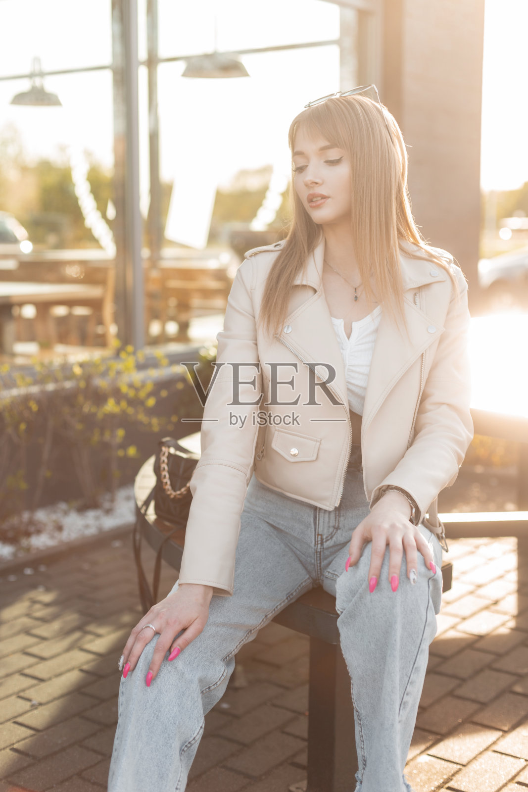 时尚美丽的年轻潮女孩,穿着时髦的摇滚风格的衣服,皮夹克和牛仔裤,坐在街上咖啡馆外的长凳上,日落时分照片摄影图片