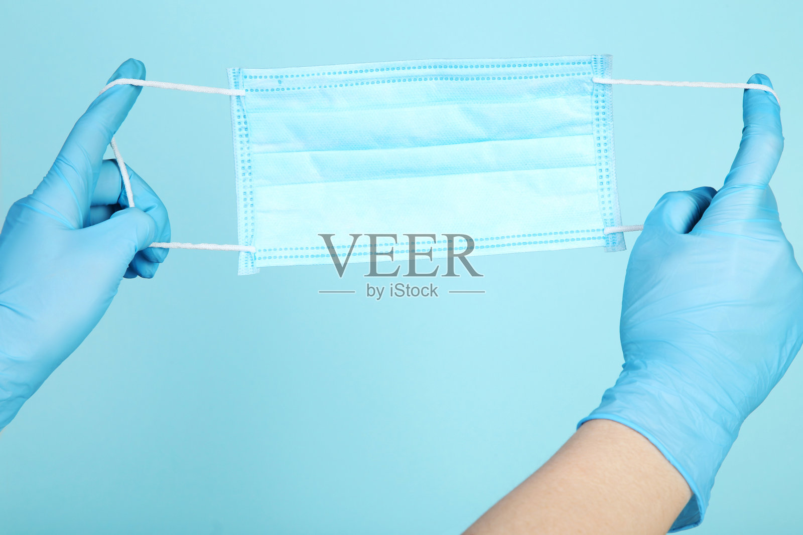 医生手戴手套,手里拿着蓝色背景的医用口罩照片摄影图片