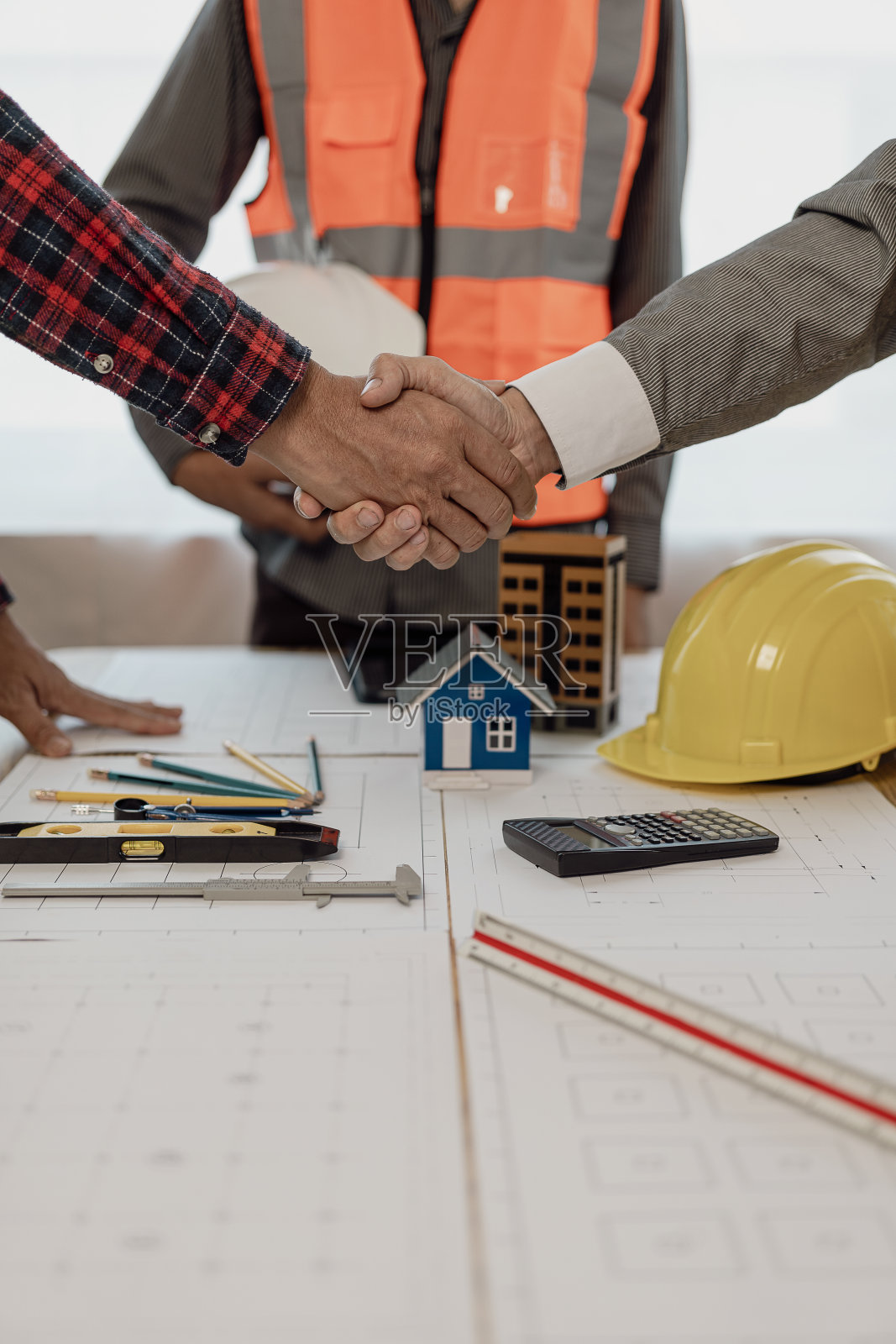 建筑师和施工工程师在办公室施工现场完成协议后手拉手进行团队合作和合作理念的特写照片,房屋平面图放在桌子上照片摄影图片