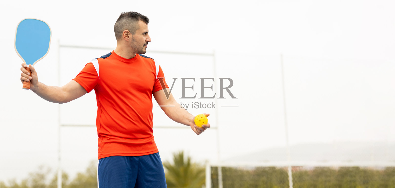 一个穿着运动服的成年男子正在玩匹克球。这个年轻人准备在比赛中发球。广告文案空间。泡菜球。照片摄影图片