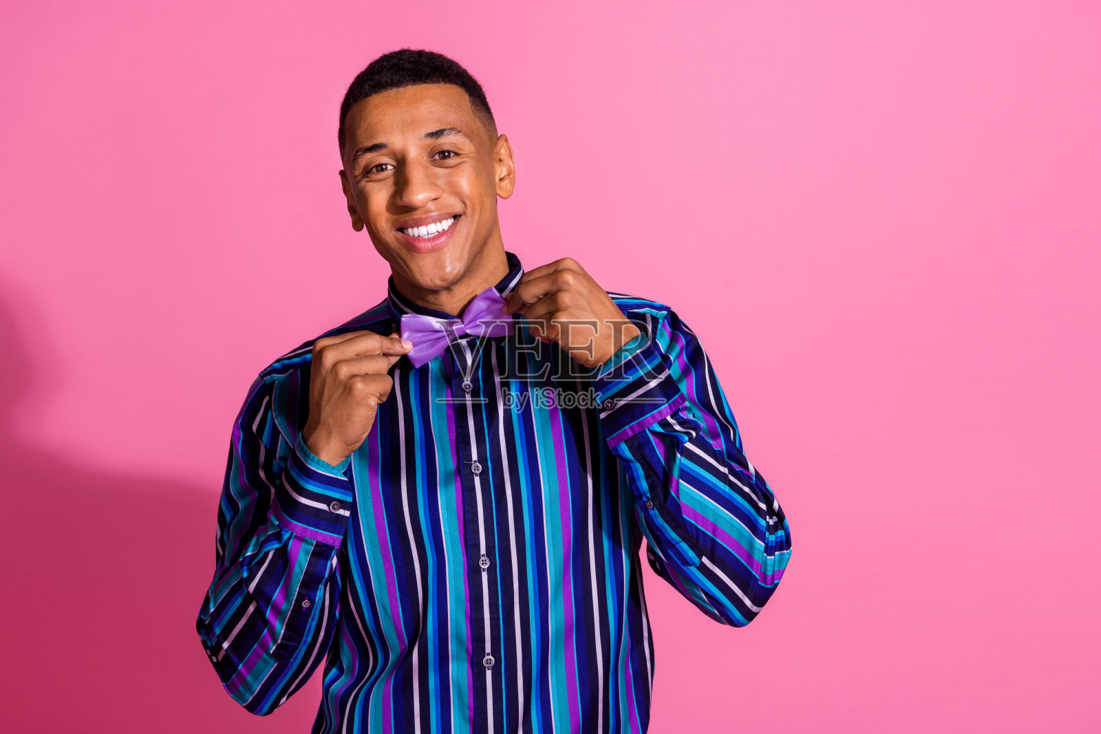 照片开朗积极的家伙穿着条纹衬衫调整领结看起来空的空间孤立的粉红色背景照片摄影图片