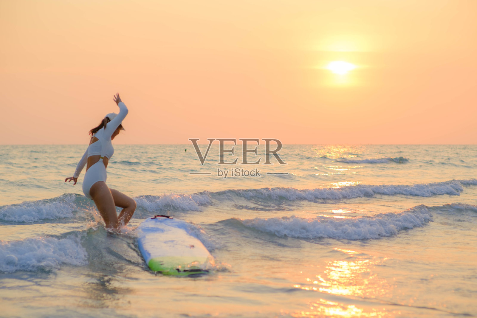 美丽的亚洲女人站在海边冲浪在日落与美丽的橙色辉光。照片摄影图片