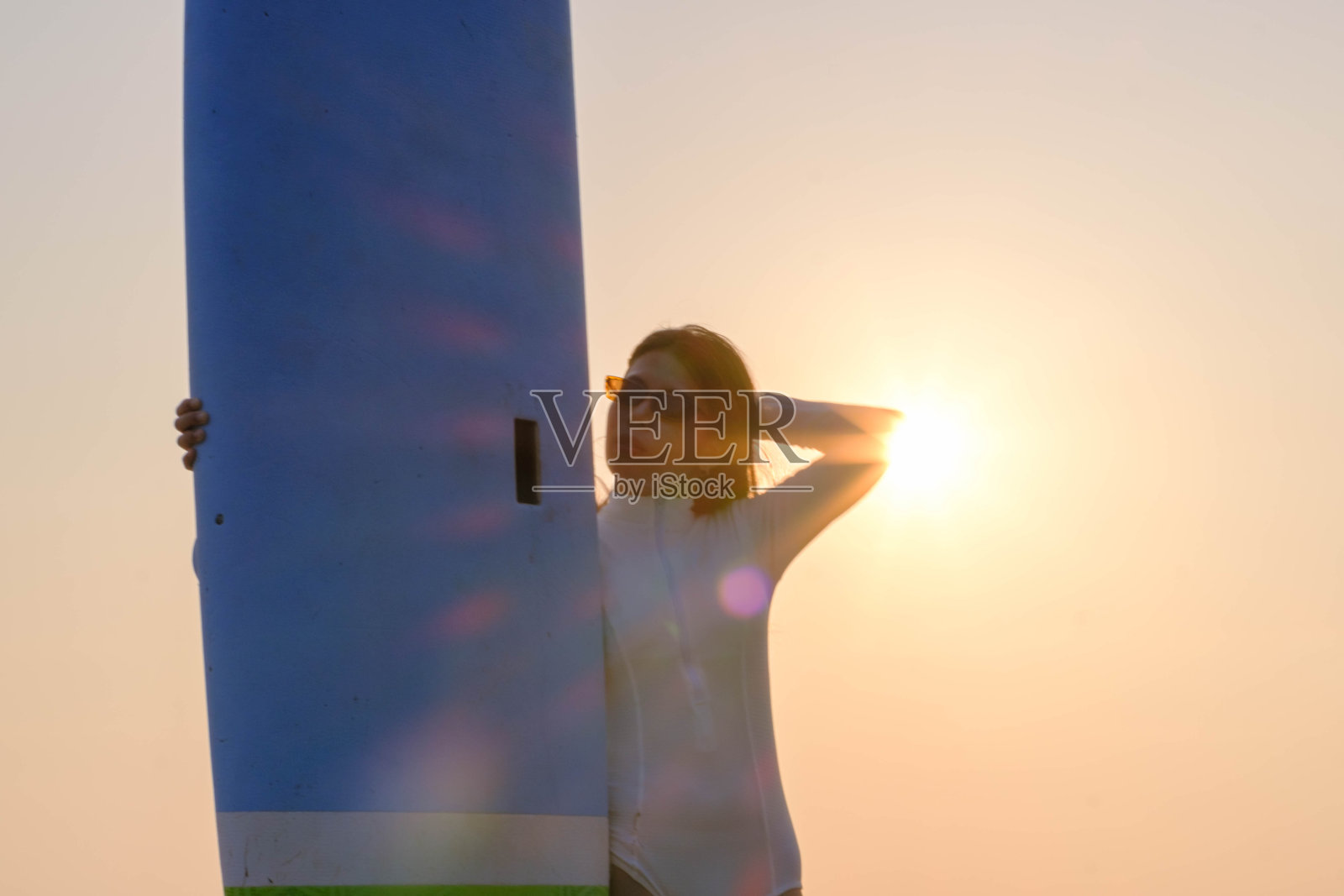 日落时分,年轻的亚洲女子站在海边的冲浪板上照片摄影图片