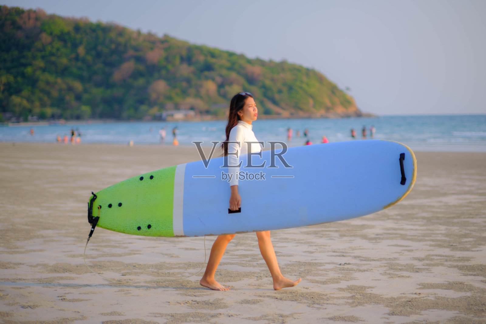 日落时分,年轻的亚洲女子在海边沙滩上拿着冲浪板散步照片摄影图片