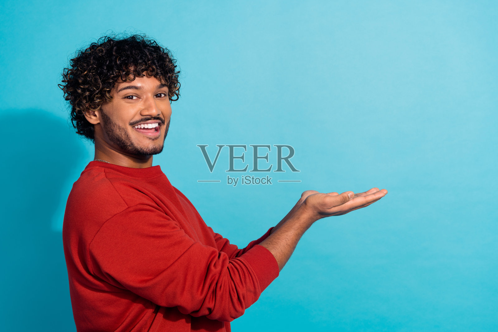 英俊男子的侧面肖像,牙齿微笑,双臂抱空,提供孤立的蓝色背景照片摄影图片